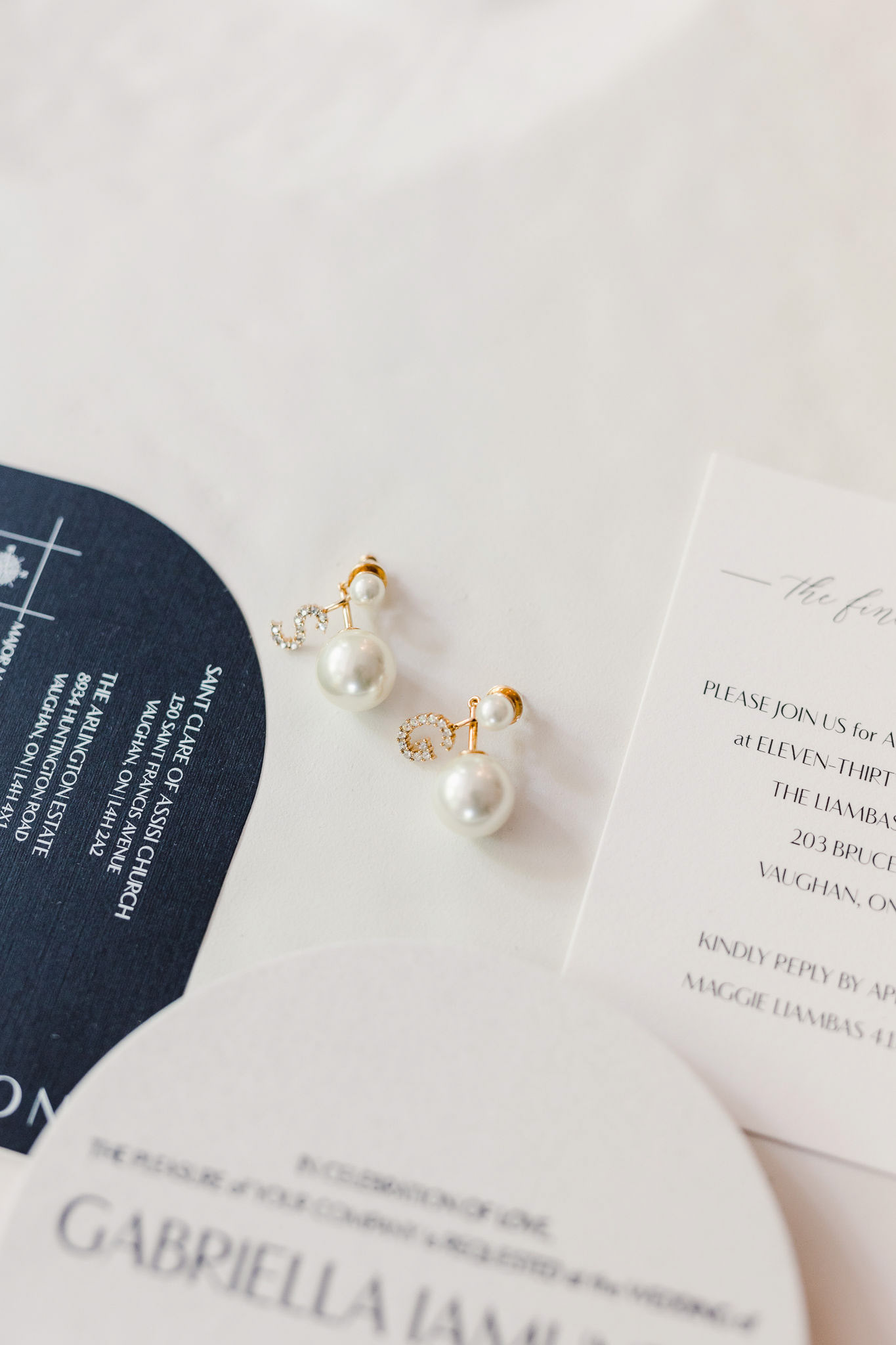 Pearl stud earrings and a wedding invitation on a white table.