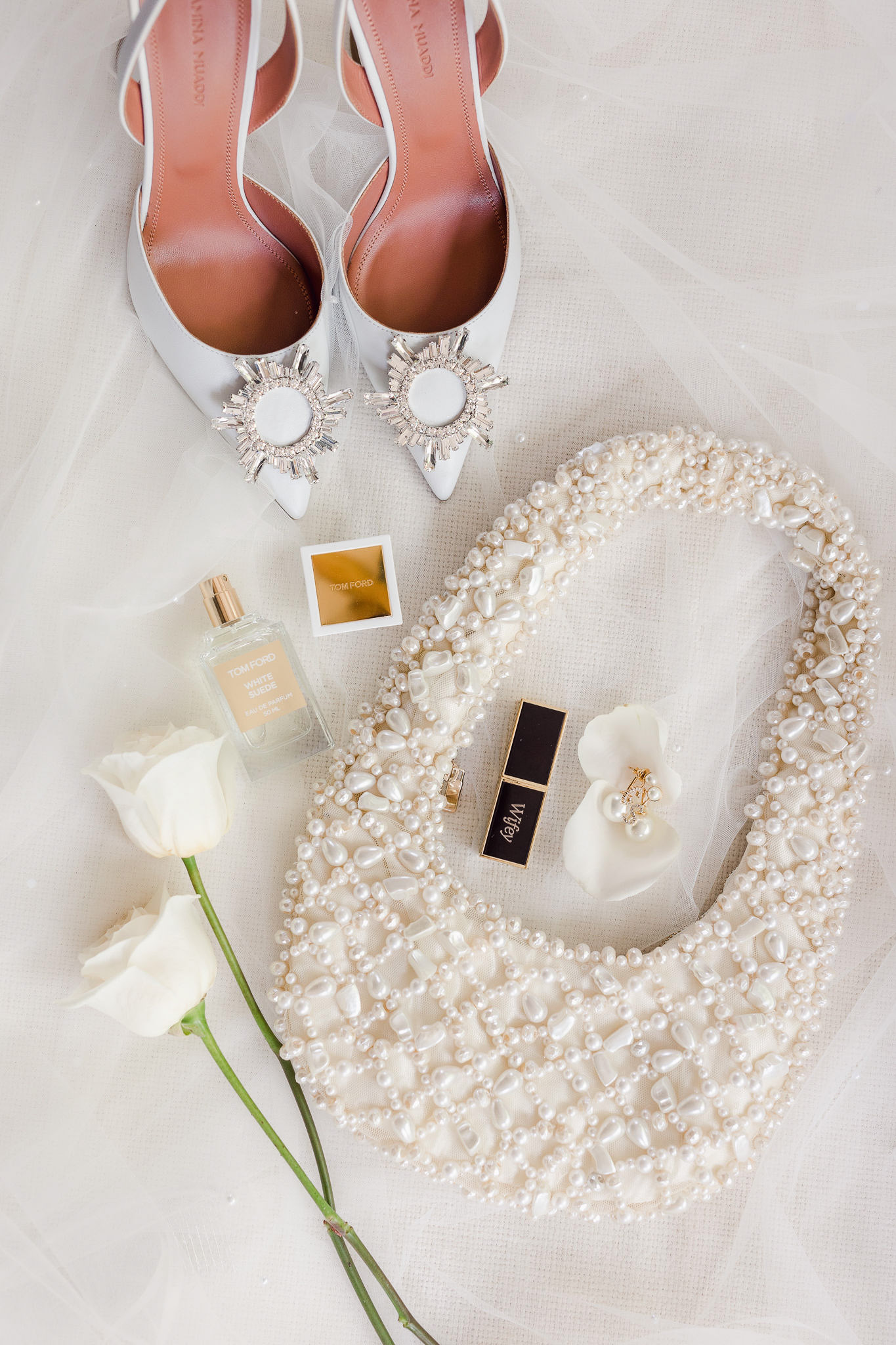 A white purse, shoes and flowers are laid out on a white table.