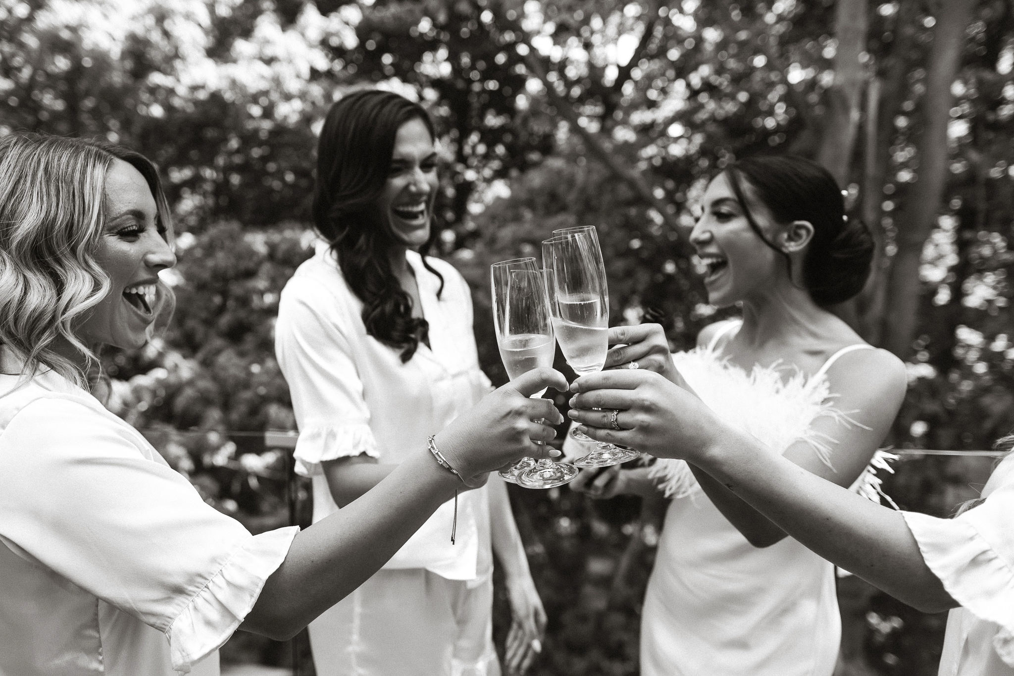 Four bridesmaids in white robes standing on a deck with champagne