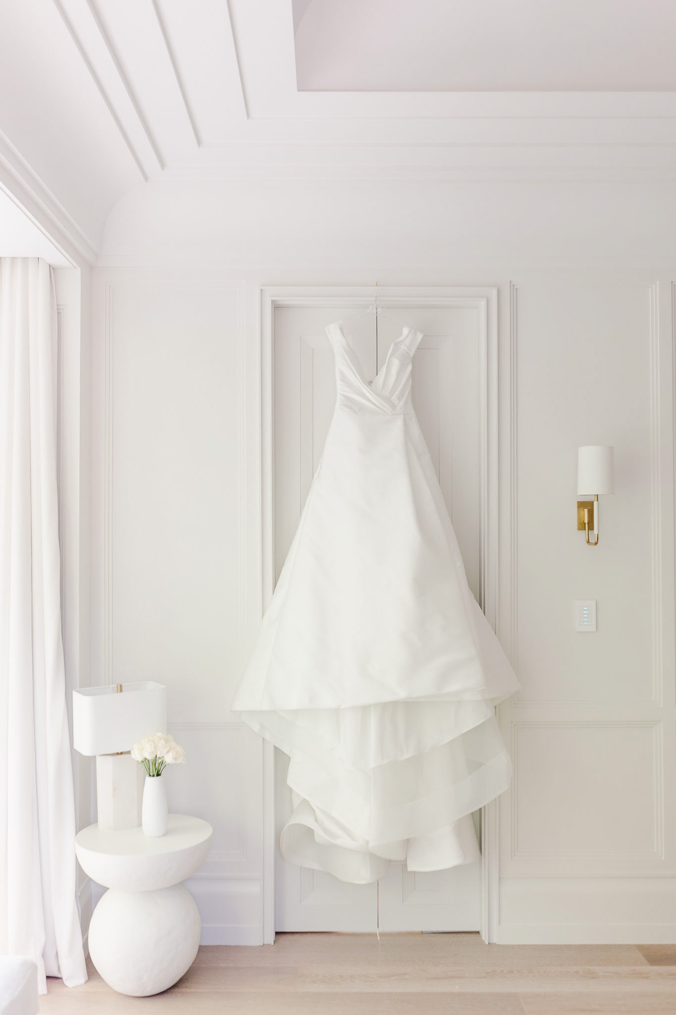 A wedding dress hangs in a white room.