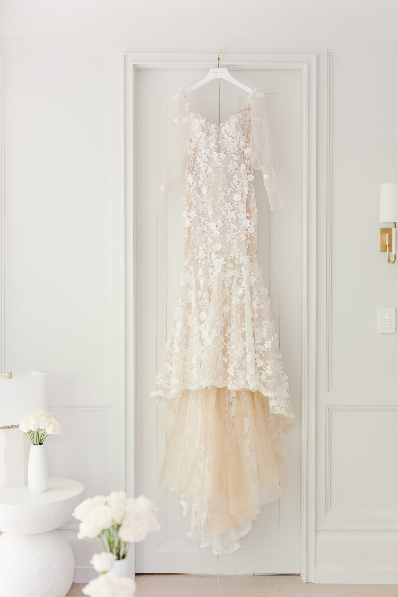 A reception wedding dress hangs in a white room.