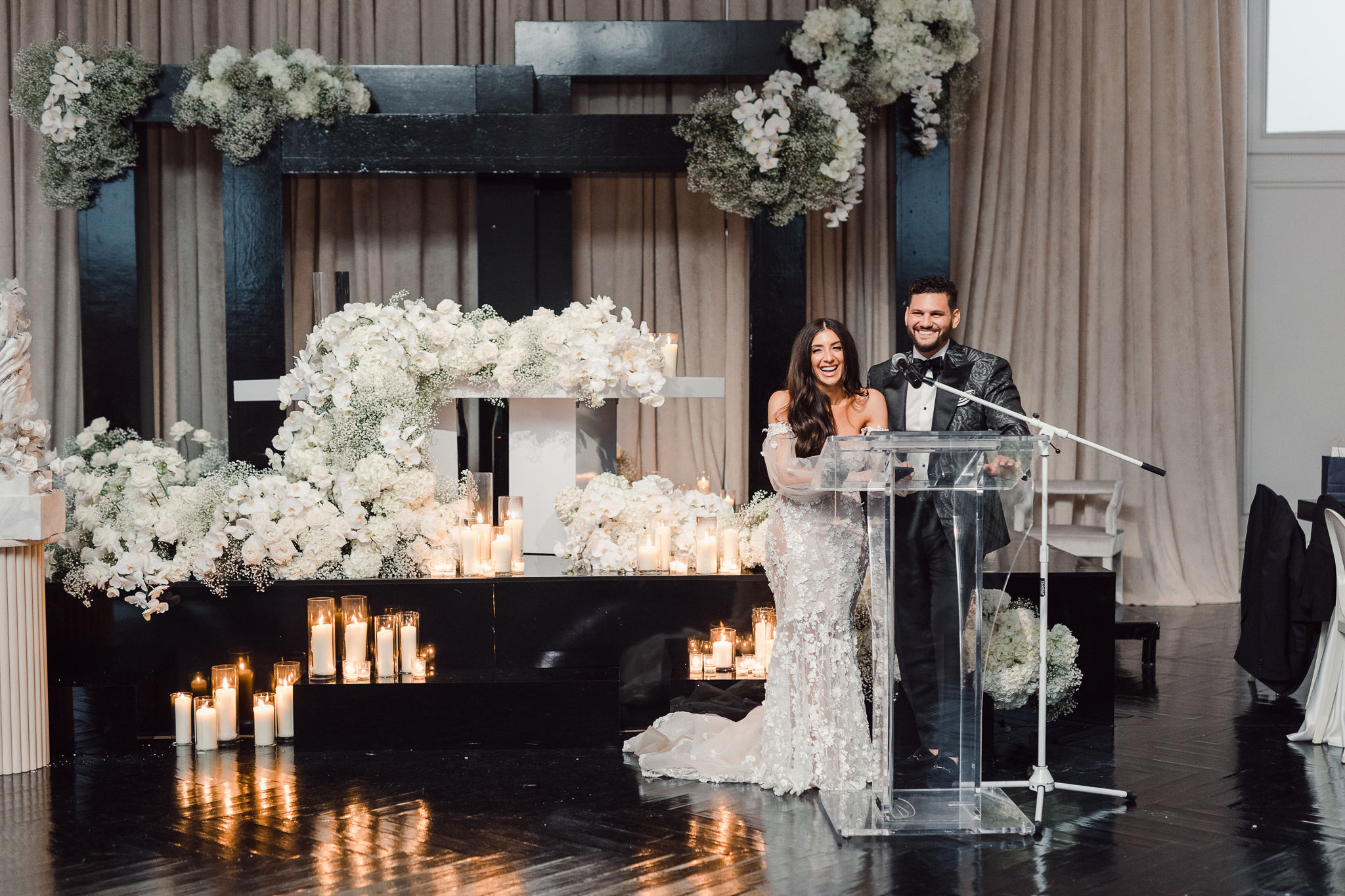 A reception speech with a bride and groom standing at a podium in front of candles and floral arrangements.