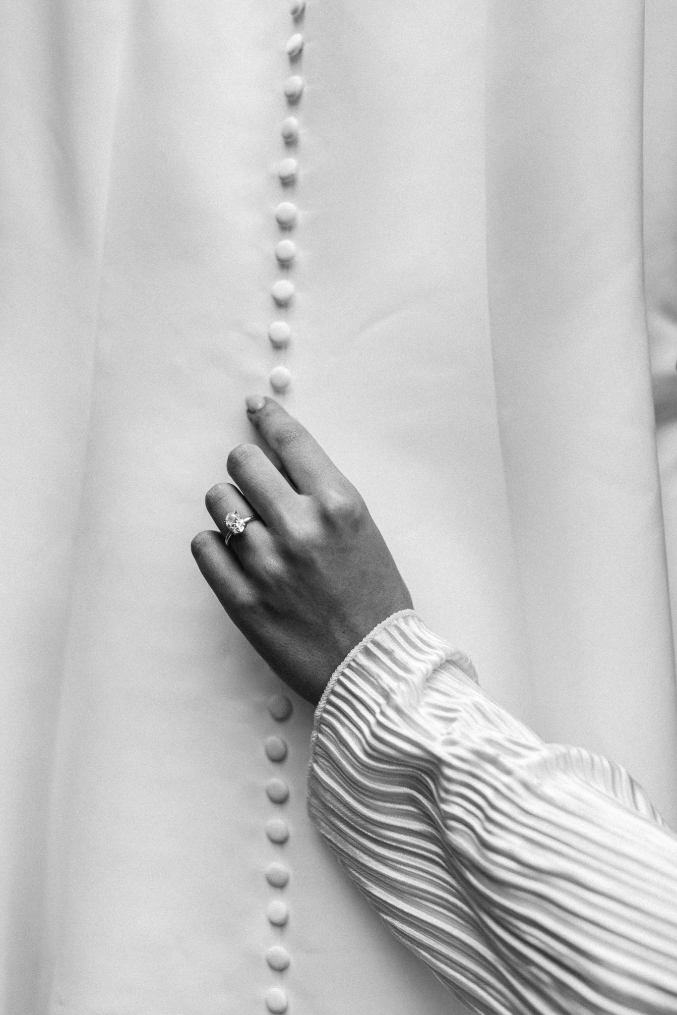 A close-up of a bride's hand delicately touching the fabric of her wedding dress against a wall.
