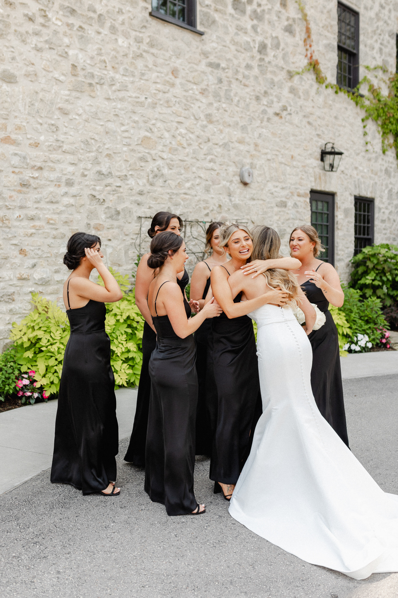 Bridesmaid hugging the bride after bride reveal in front of a stone wall.