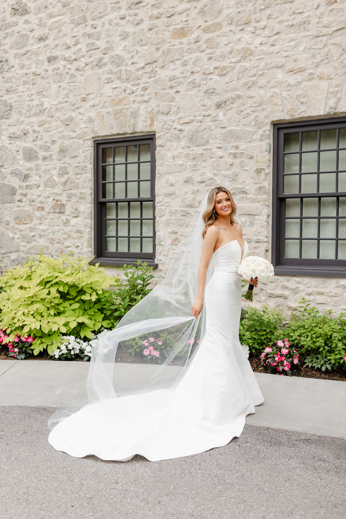 A bride in a white wedding dress posing elegantly in front of a stone building