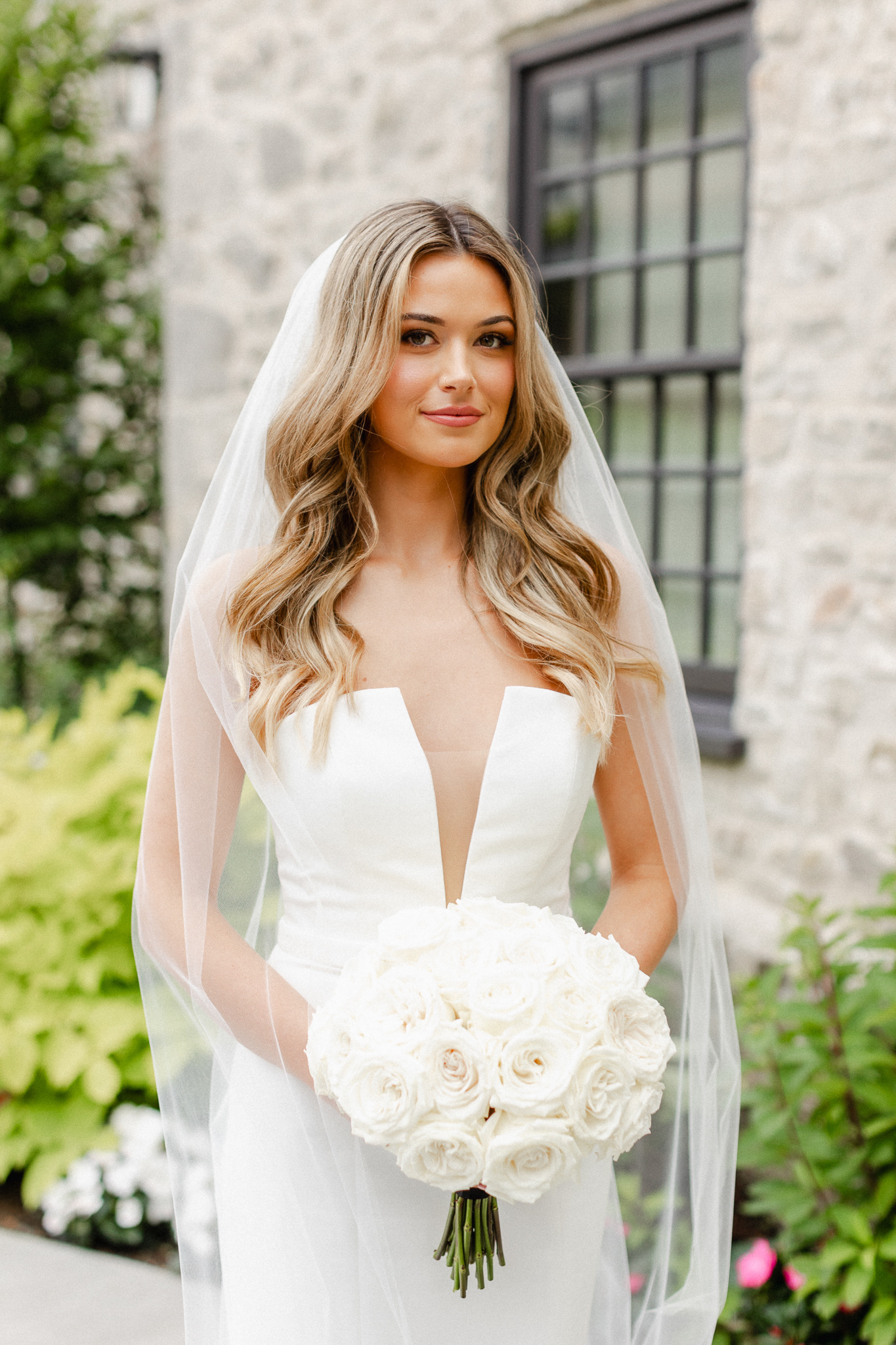 A stunning bride, elegantly dressed in white, gracefully holds a bouquet in this captivating bridal portrait.