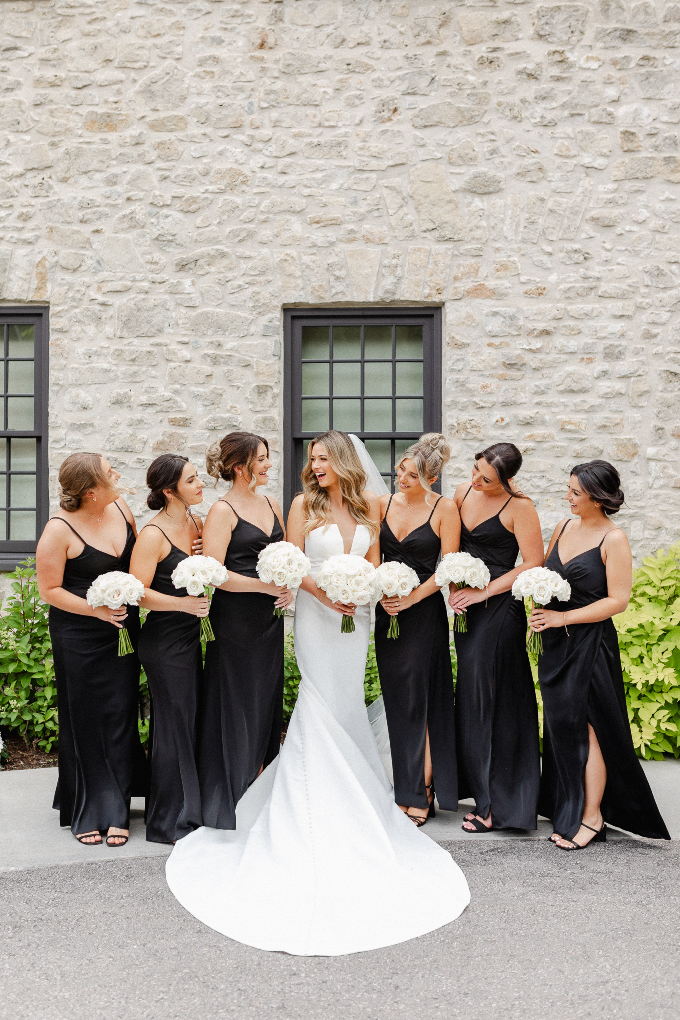 Bridesmaids elegantly dressed in black attire, holding beautiful white bouquets with the bride.