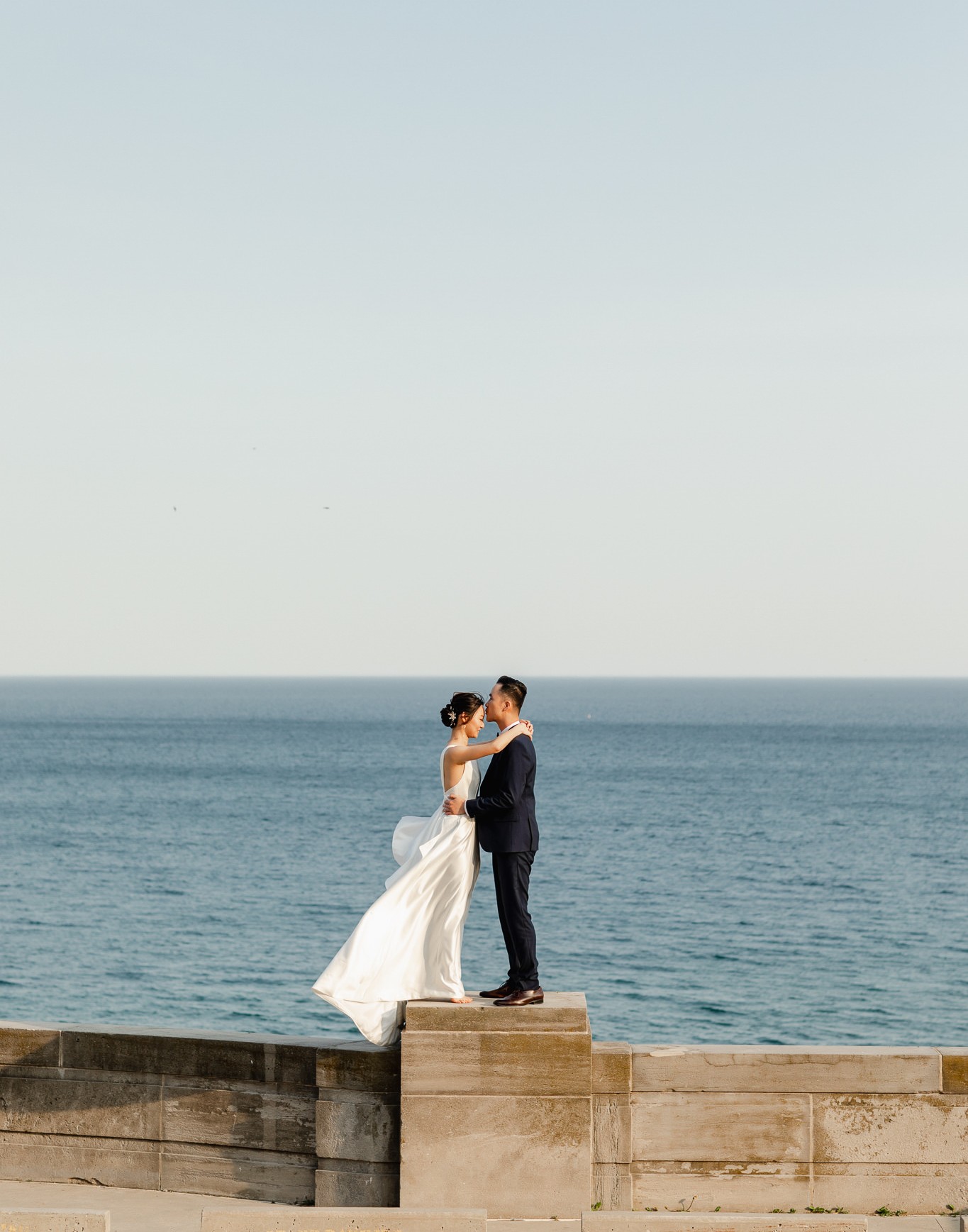 Wedding photographer capturing a couple's engagement session pose by lakefront.