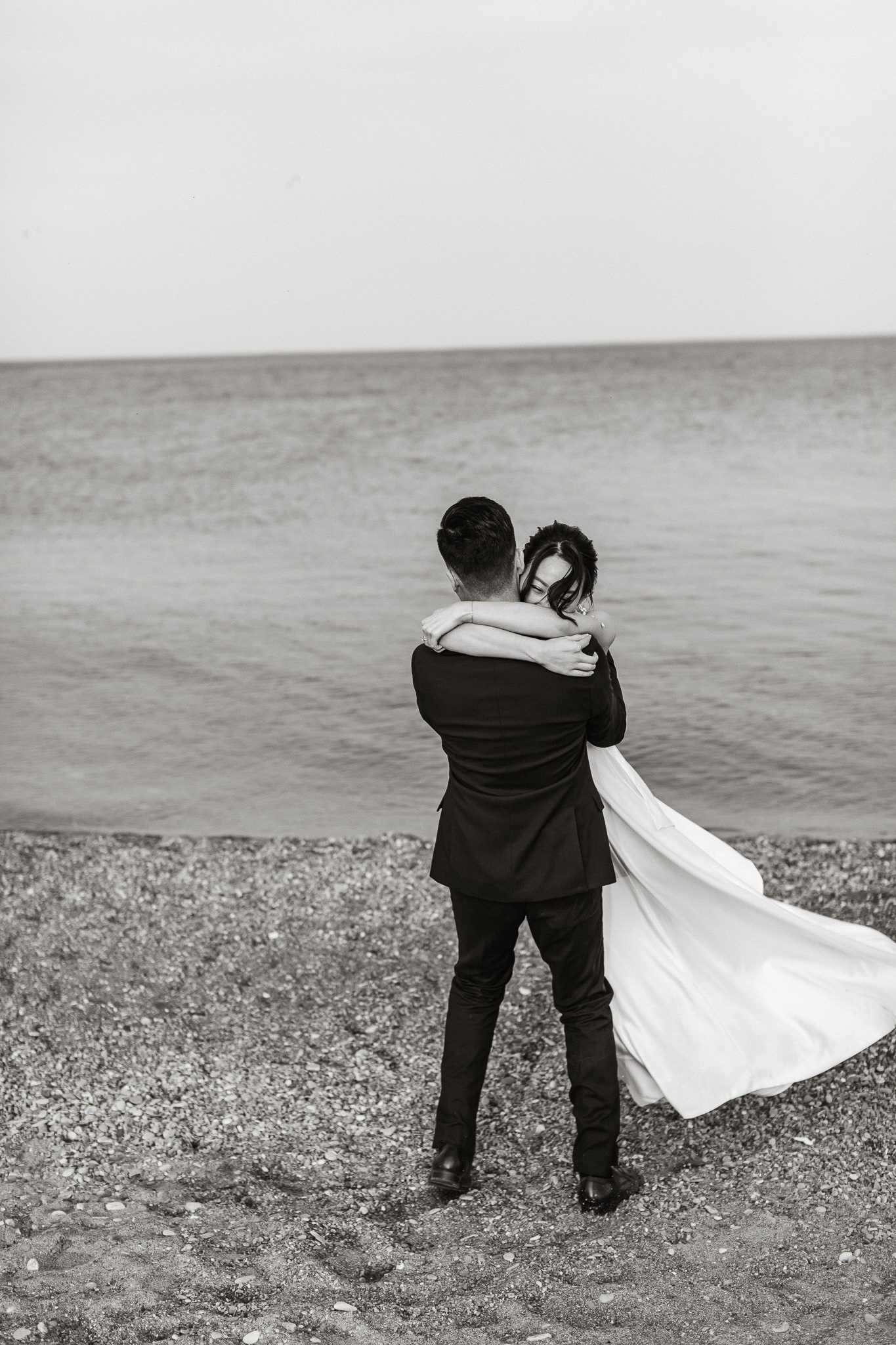 Wedding photographer capturing a couple's engagement session pose by lakefront.