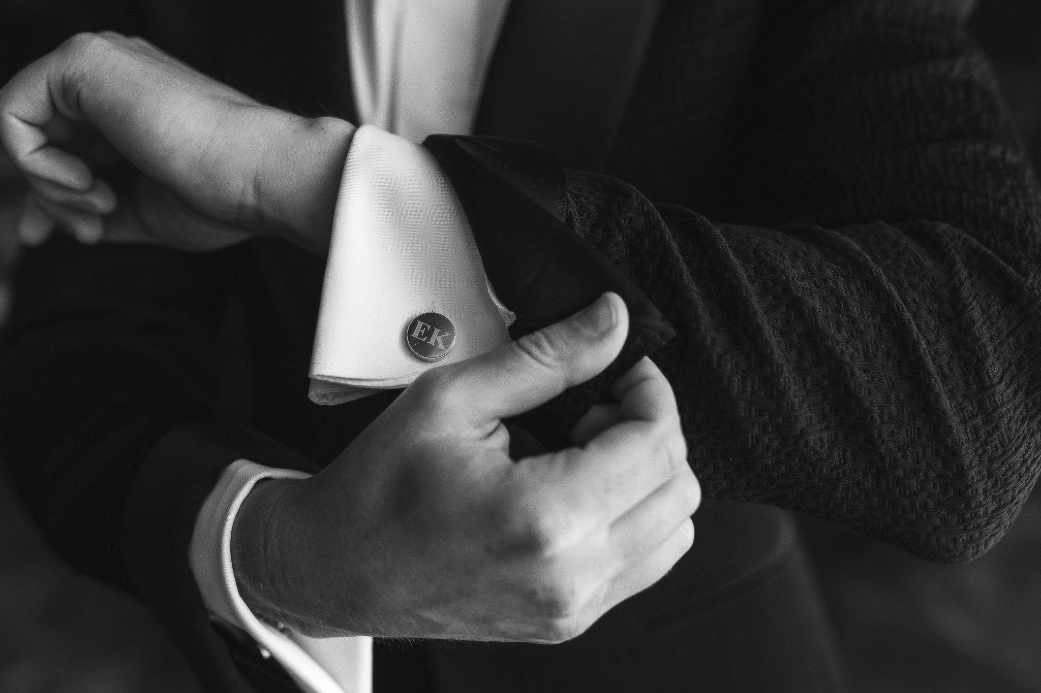 Close-up of groom holding his custom cuff-link with initials "EK"
