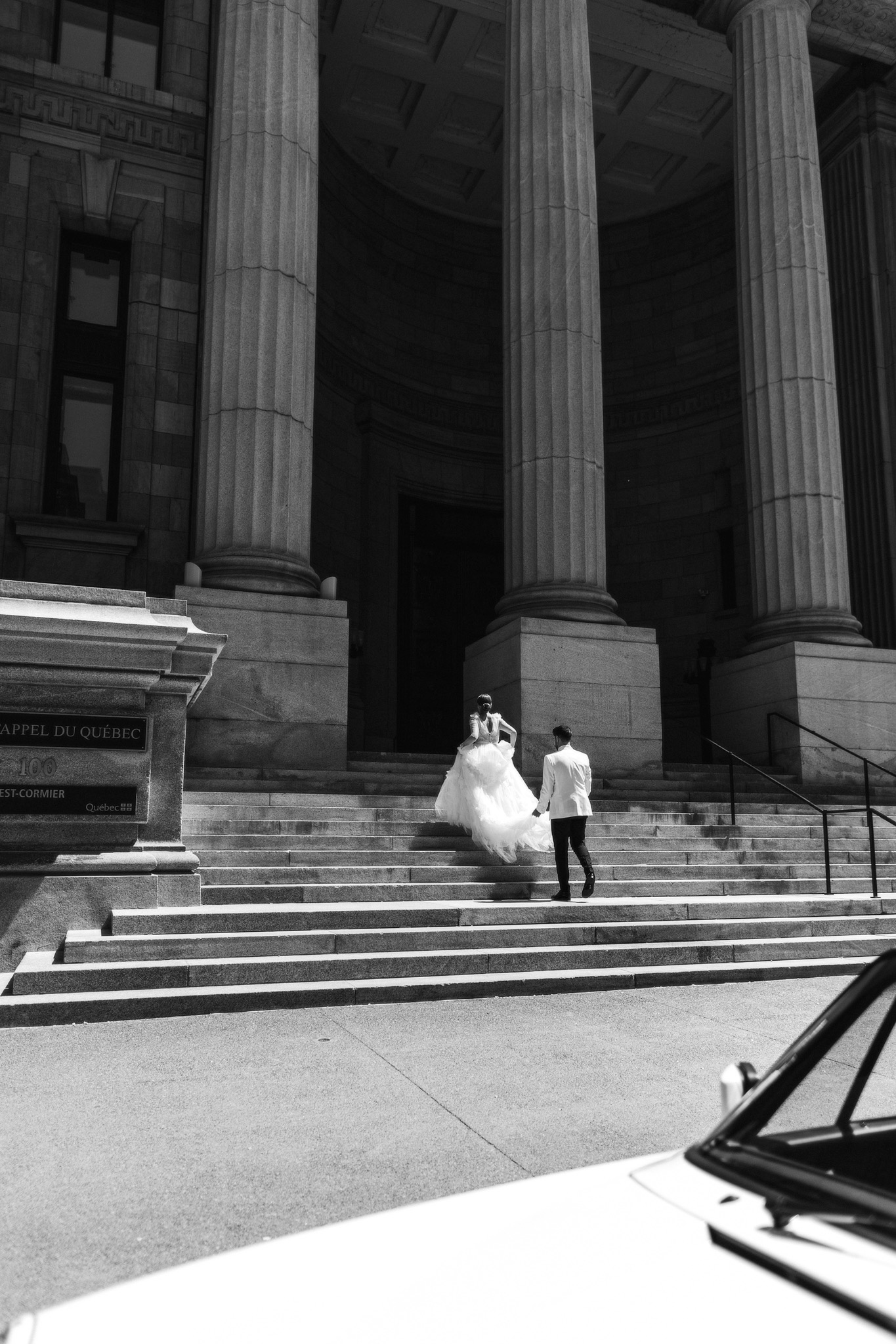 Bride and groom running up the steps of a grand cathedral, captured in black and white in a photojournalistic, editorial wedding style