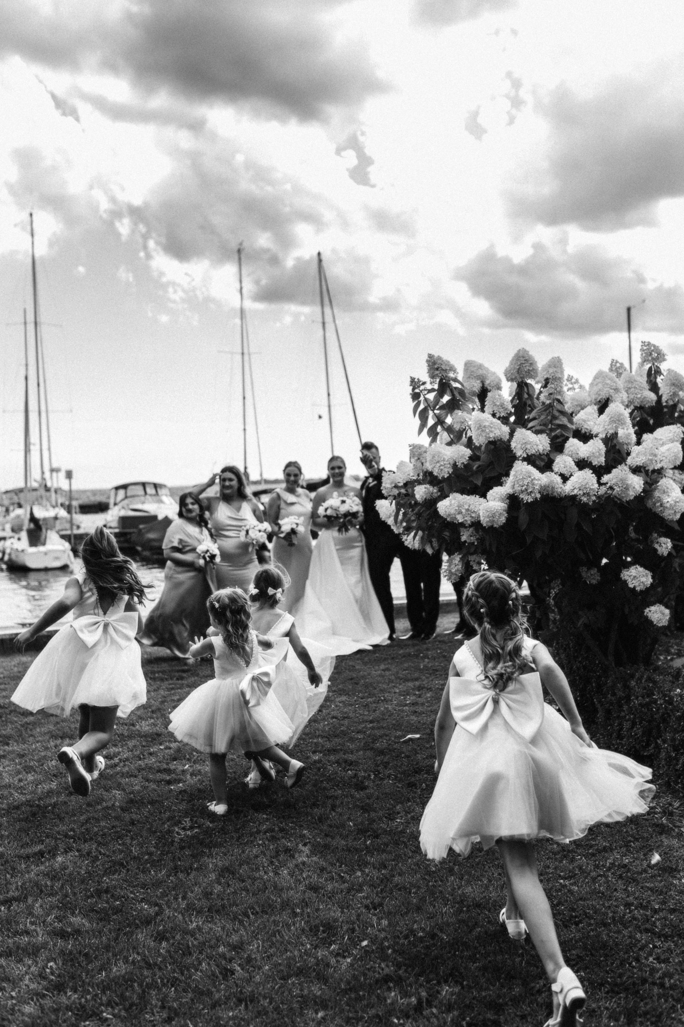 Photojournalistic wide shot of flower girls running toward the bride and groom outdoors, capturing spontaneous movement and celebration during a wedding