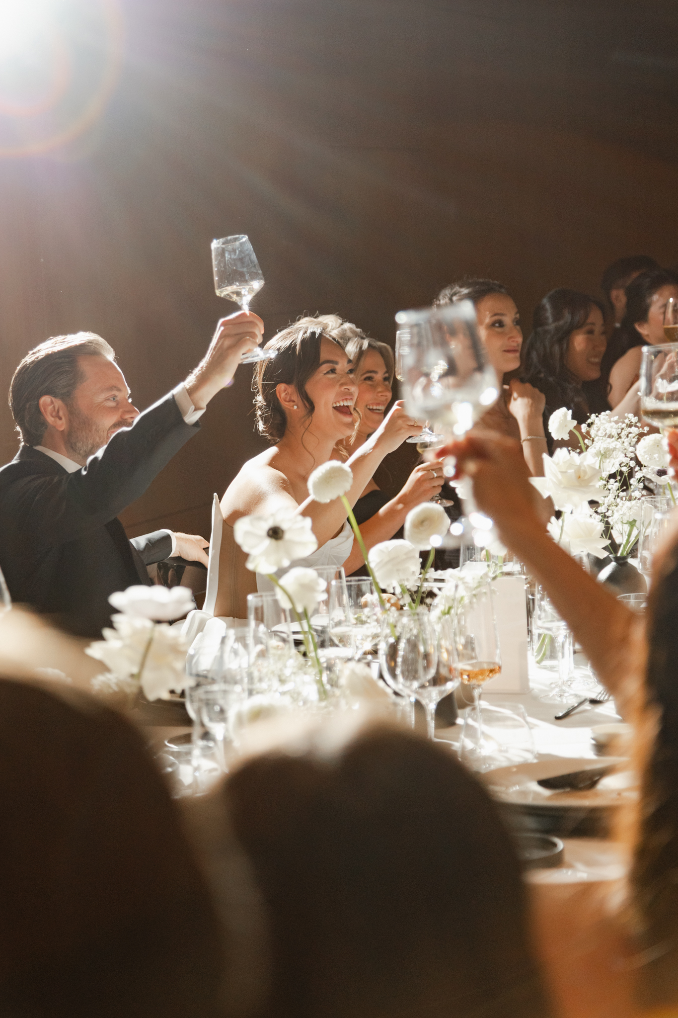 Wedding guests raising glasses and laughing during a heartfelt toast, captured in a candid, unposed moment at the reception.