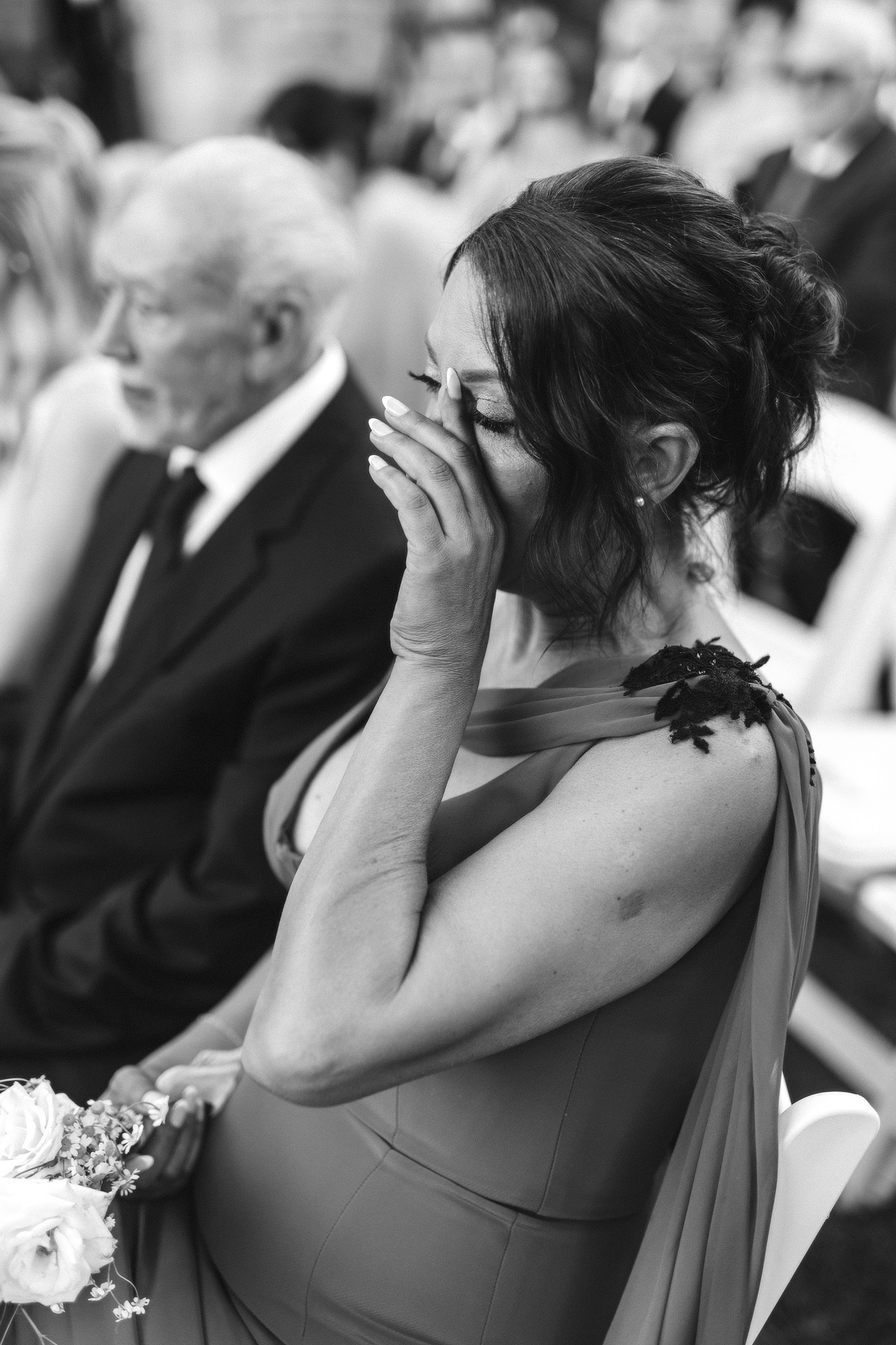 Mother of the bride wiping away tears during the wedding ceremony, captured in black and white in a candid, photojournalistic moment.