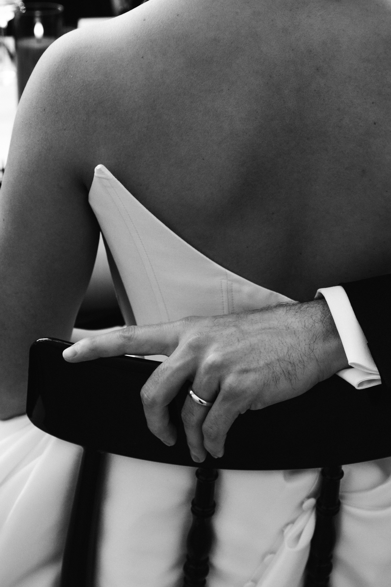 Candid black and white close-up of a groom’s hand resting on the bride’s back during an intimate wedding moment.