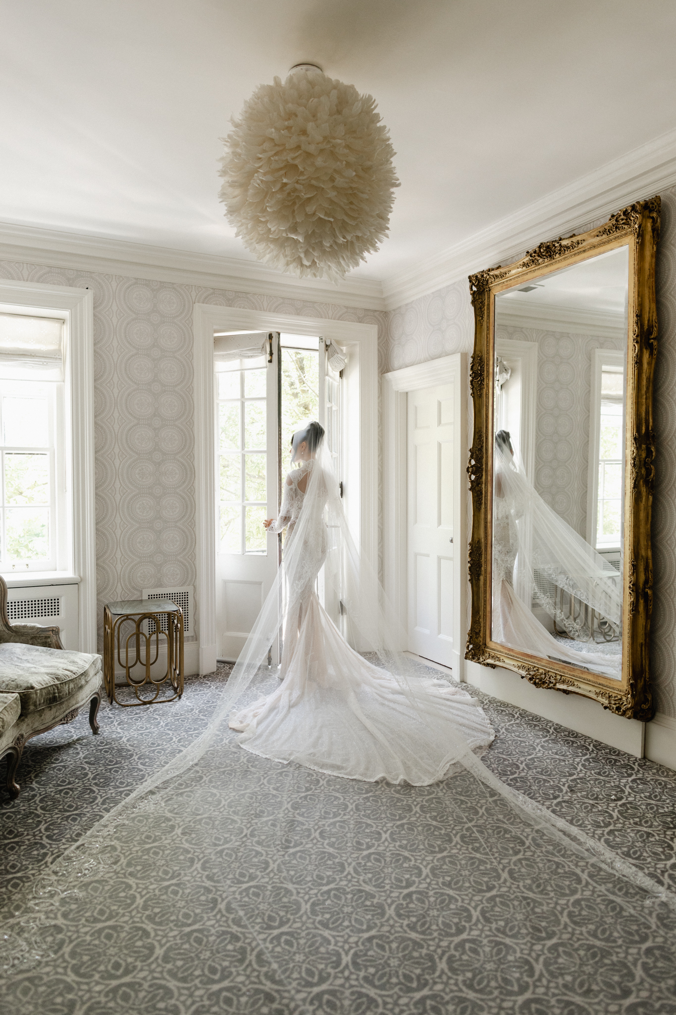 Bride standing in front of a large mirror with her veil flowing behind her in soft natural window light, captured in an elegant, editorial bridal portrait style in Graydon Hall